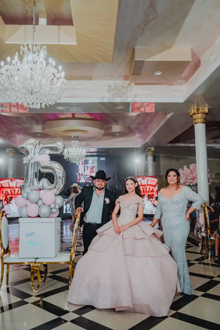 Quinceañera seated beneath crystal chandeliers at The Grand Villa ballroom